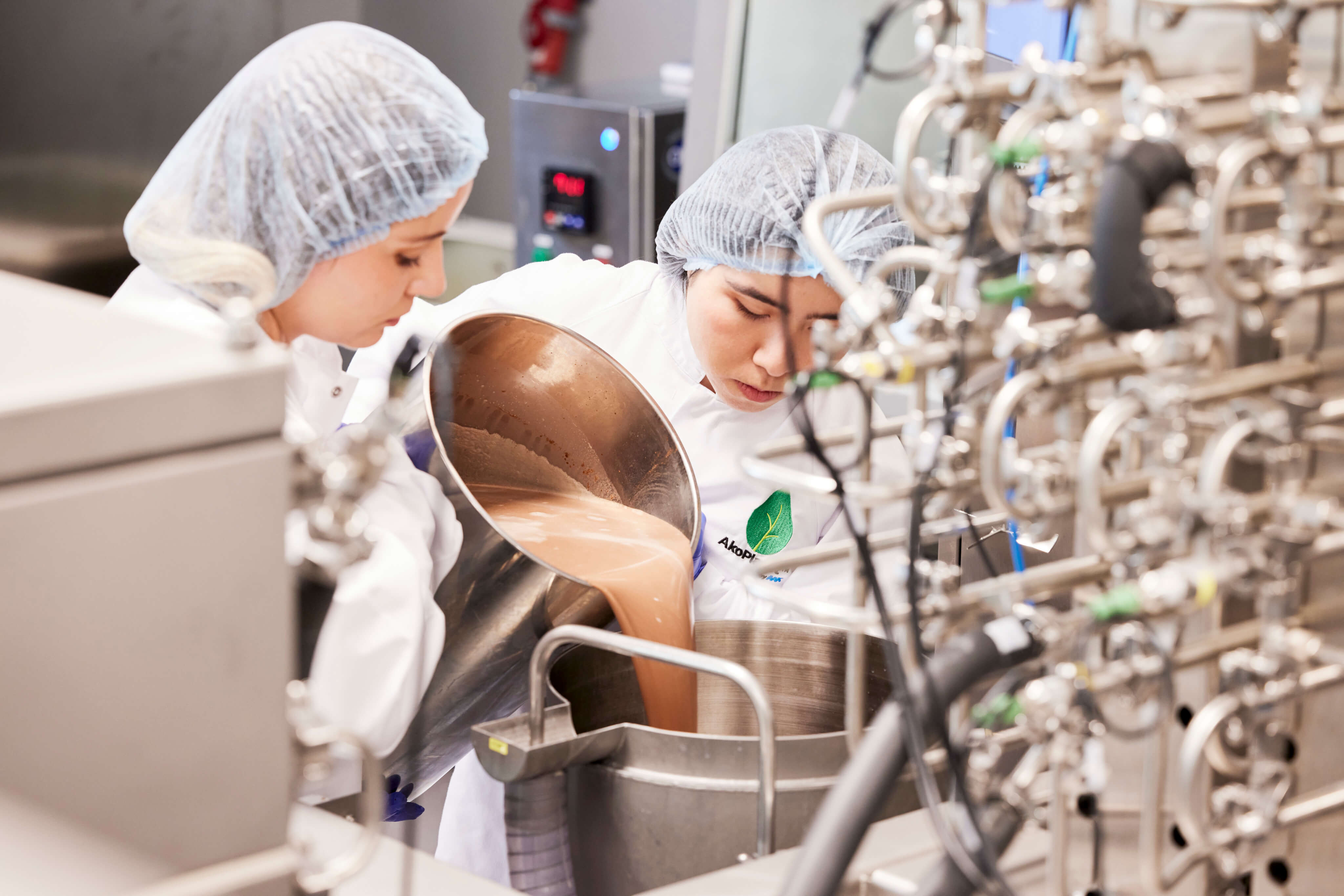 Two women in white lab coats working together in a factory, focused on their tasks.