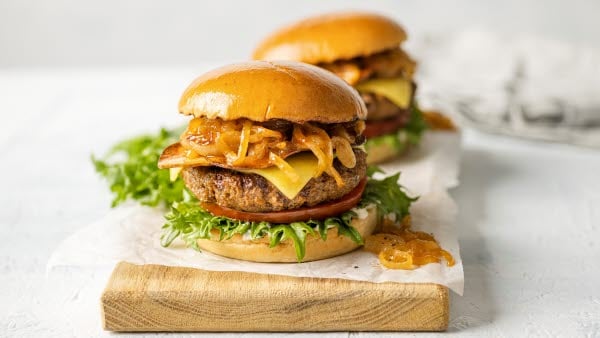 Two plant based meat hamburgers placed on a wooden cutting board, showcasing their toppings and fresh ingredients.