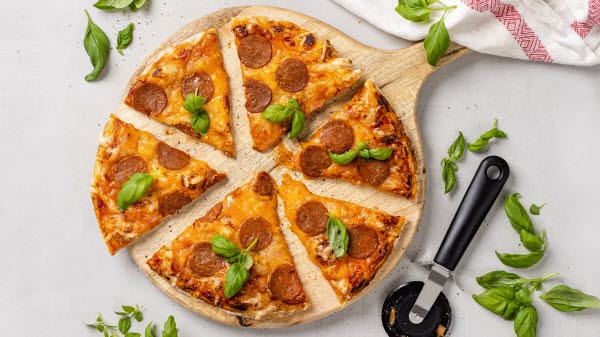 Sliced pepperoni pizza topped with fresh basil, presented on a rustic wooden board.