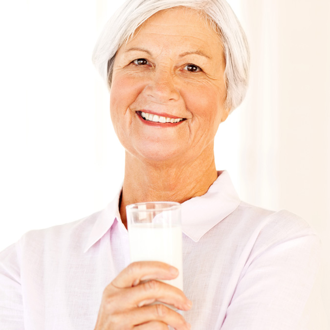 Older woman smiling and holding a glass of milk - Special Nutrition - AAK