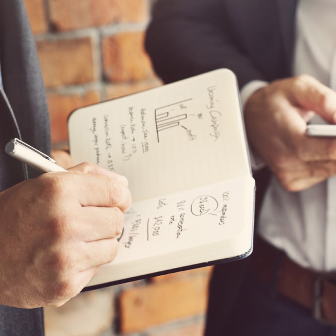 Businessmen Analysing and Writing News in a Note Book - Media - AAK